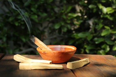 Palo santo stick smoldering in bowl on wooden table outdoors