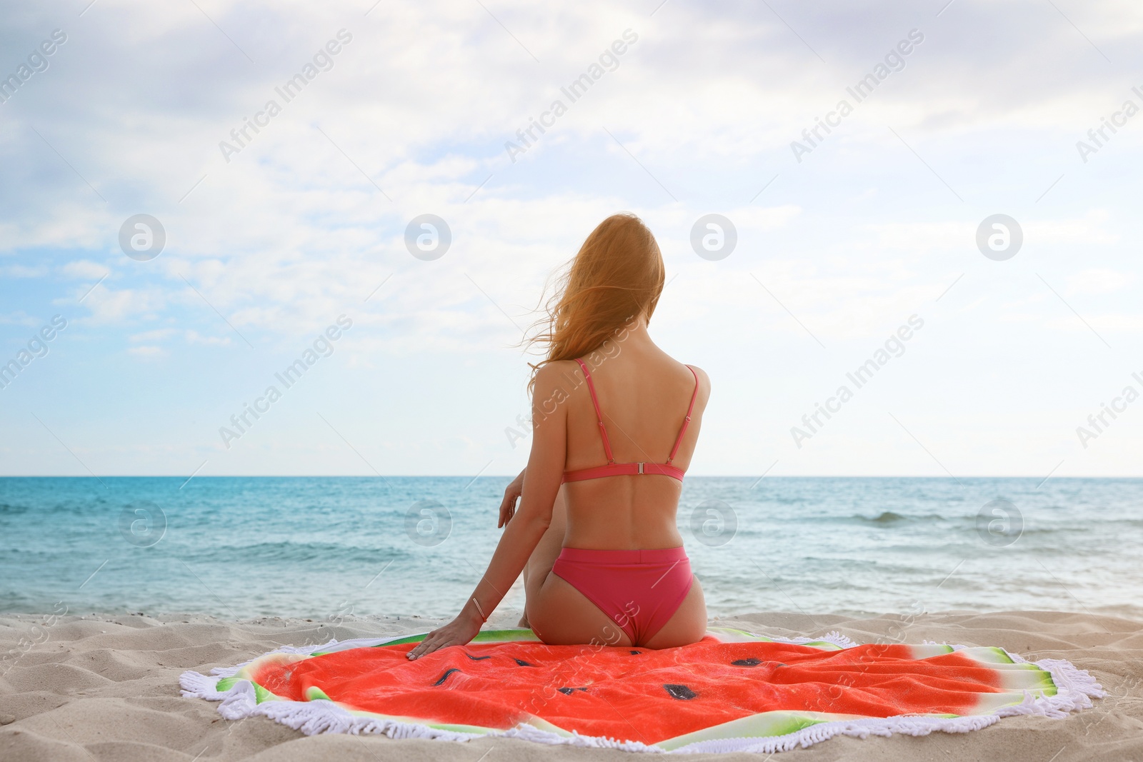 Photo of Beautiful woman sitting on beach towel near sea, back view