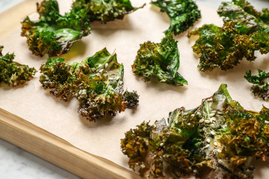 Photo of Tasty baked kale chips on wooden board, closeup