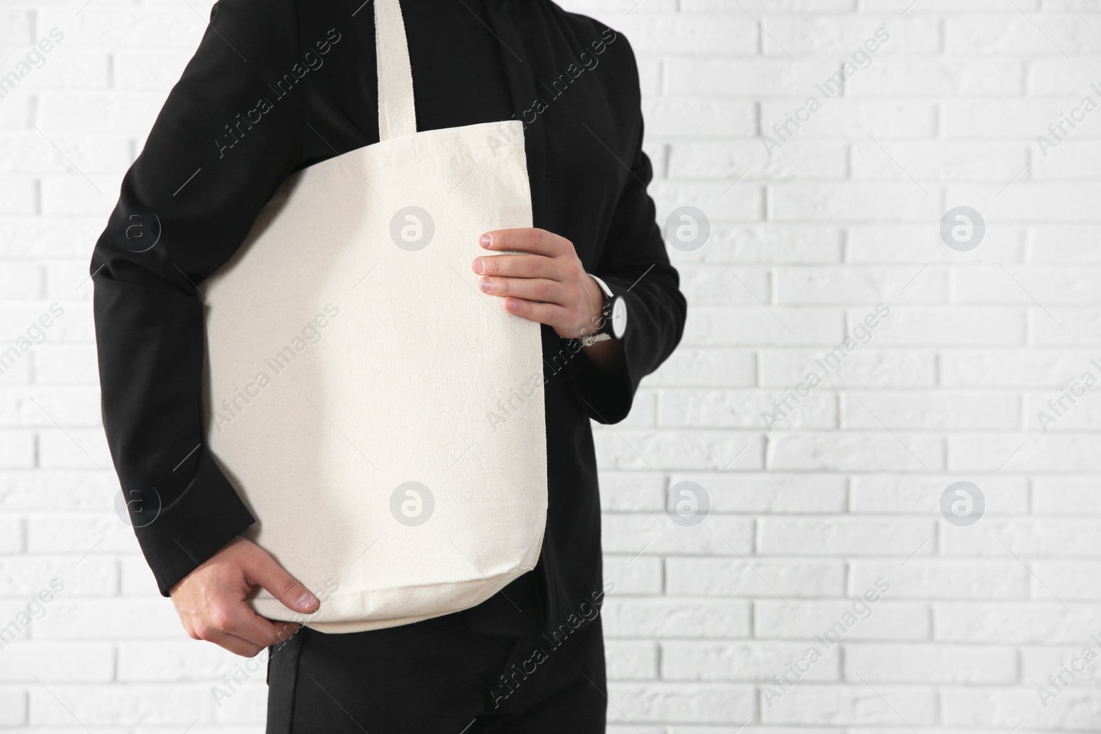 Photo of Young man holding textile bag against brick wall, closeup.  Mockup for design
