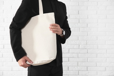 Photo of Young man holding textile bag against brick wall, closeup.  Mockup for design