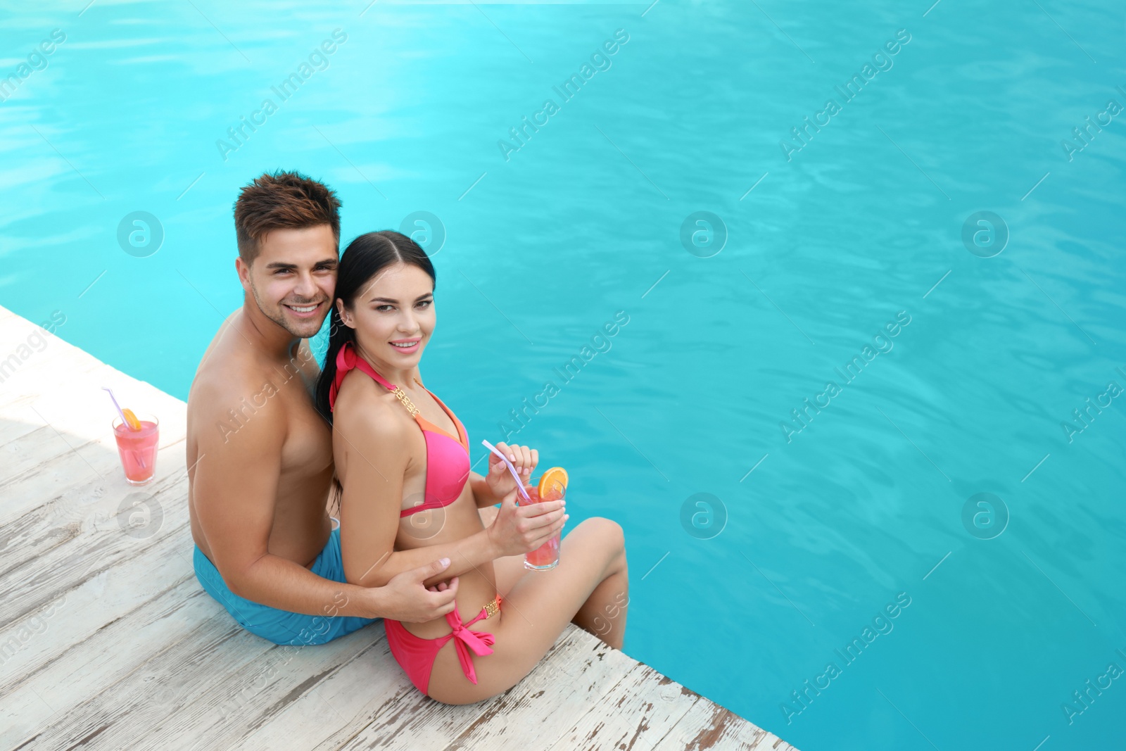 Photo of Woman in bikini with boyfriend near outdoor pool. Happy young couple