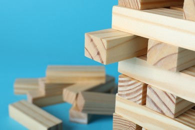 Photo of Jenga tower made of wooden blocks on light blue background, closeup. Space for text