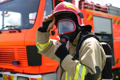 Photo of Firefighter in uniform wearing helmet and mask near fire truck outdoors