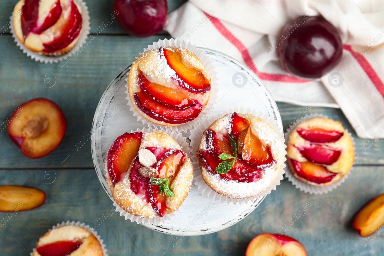 Photo of Delicious sweet cupcakes with plums on wooden stand, flat lay