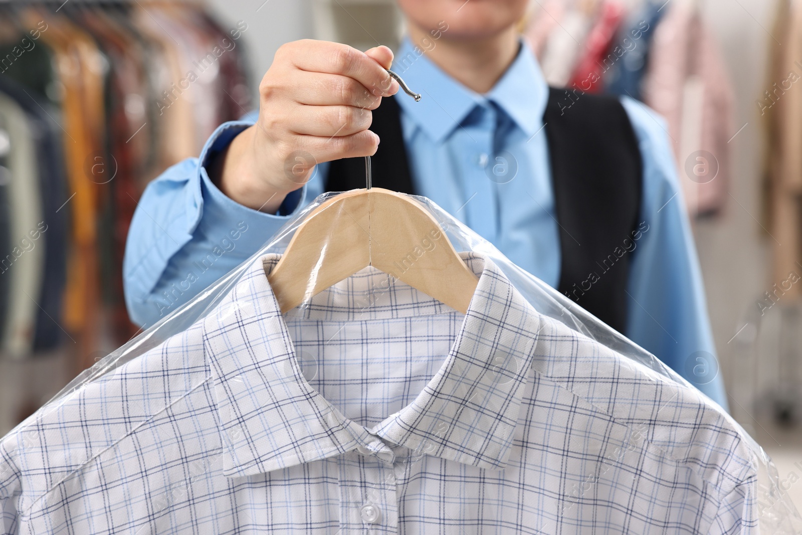 Photo of Dry-cleaning service. Woman holding shirt in plastic bag indoors, closeup