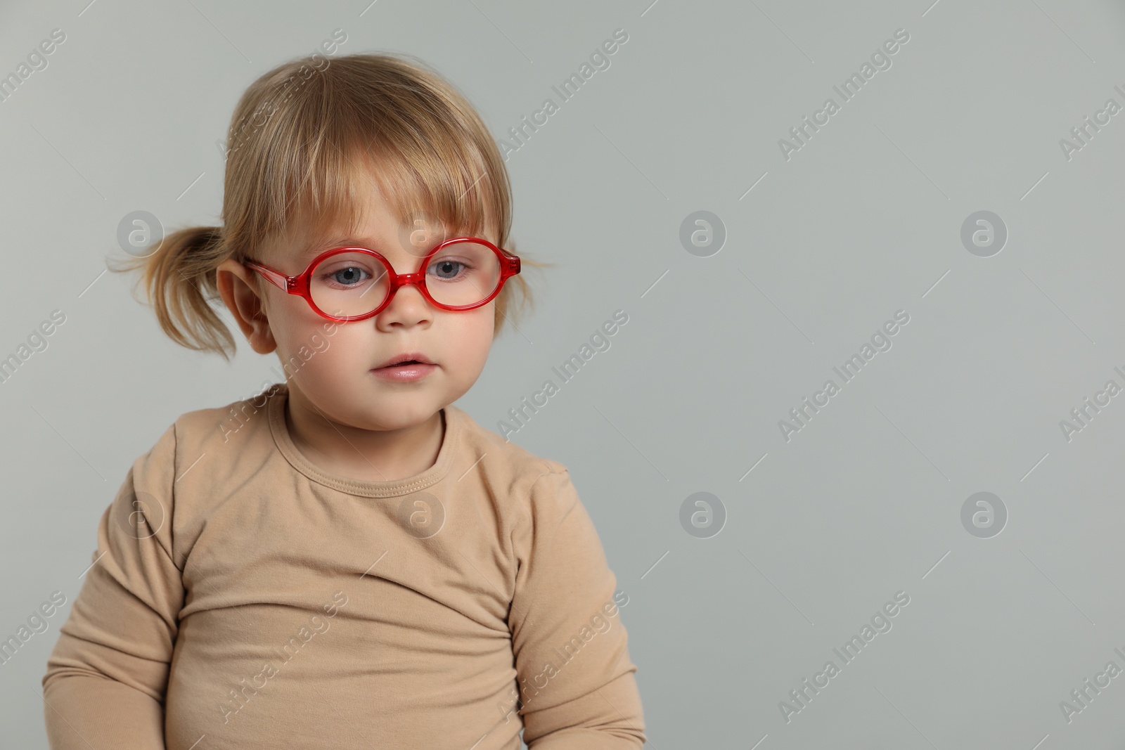 Photo of Cute little girl in glasses on light grey background. Space for text