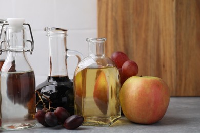 Different types of vinegar and fresh fruits on grey table