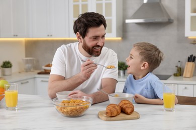 Father and his cute little son having breakfast at table in kitchen