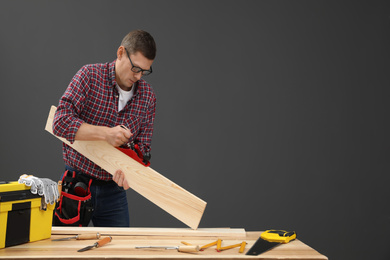 Photo of Handsome carpenter working with timber at table on black background. Space for text