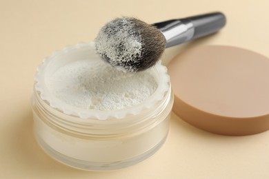 Photo of Rice loose face powder and makeup brush on beige background, closeup