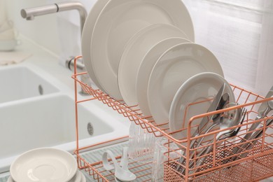 Drying rack with clean dishes on countertop near sink in kitchen, closeup