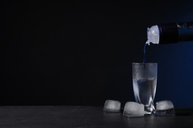 Photo of Pouring vodka from bottle into shot glass on black table against dark background. Space for text