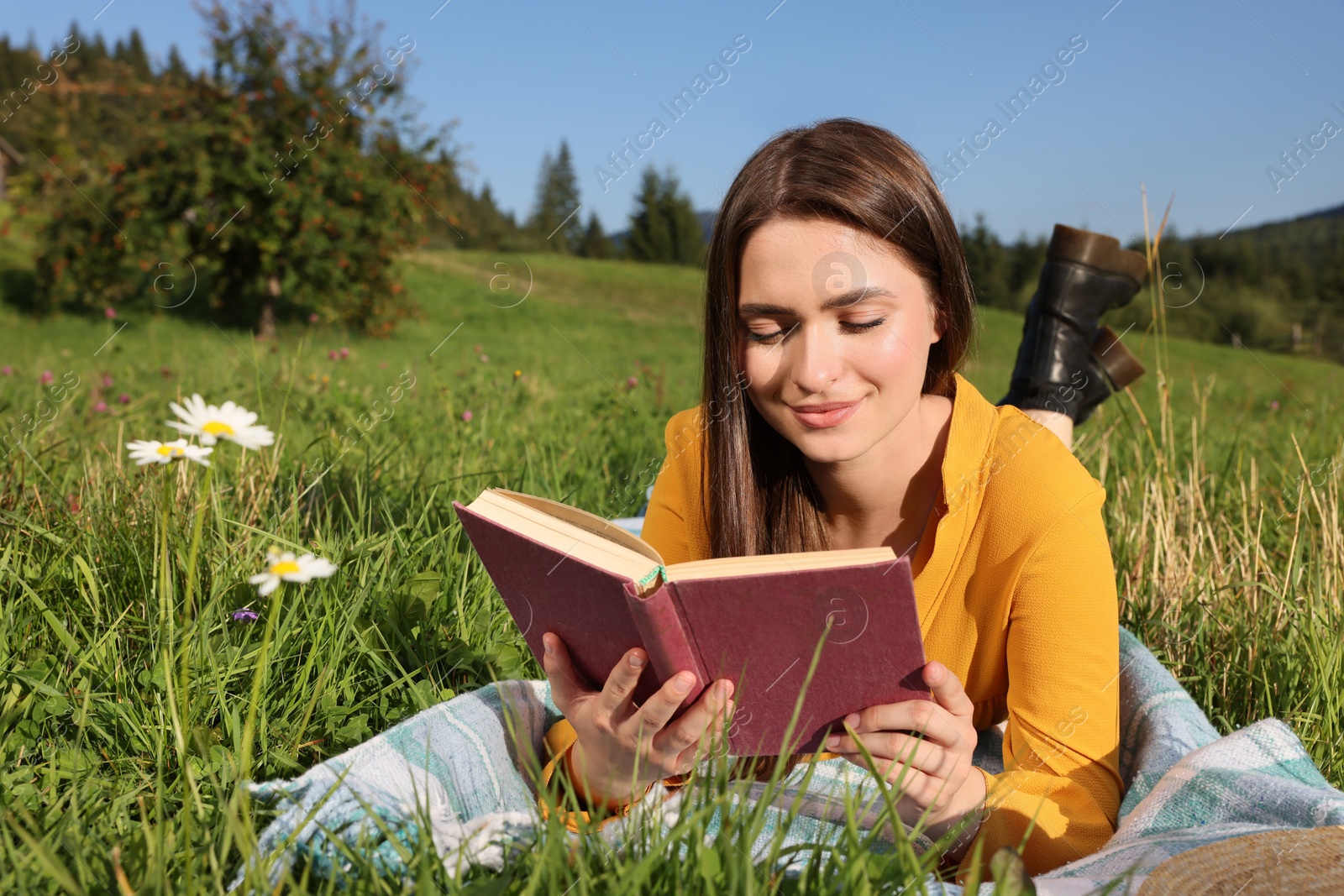 Photo of Beautiful young woman reading book on green meadow