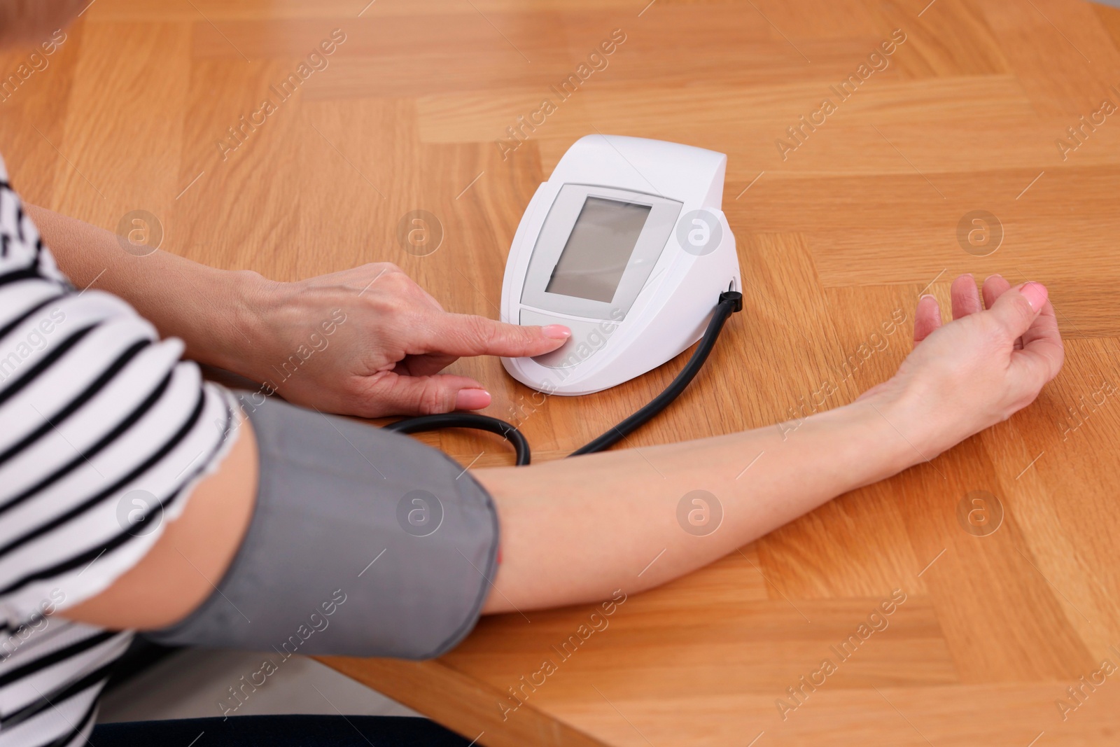 Photo of Woman measuring her blood pressure with tonometer at wooden table indoors, closeup