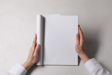Photo of Woman holding notebook with blank pages at white table, top view. Mockup for design