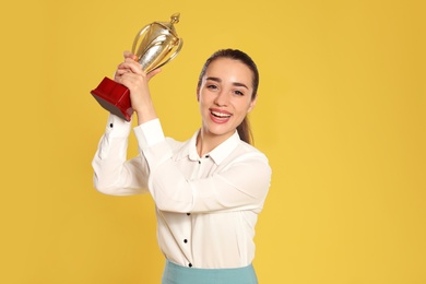 Photo of Portrait of happy young businesswoman with gold trophy cup on yellow background