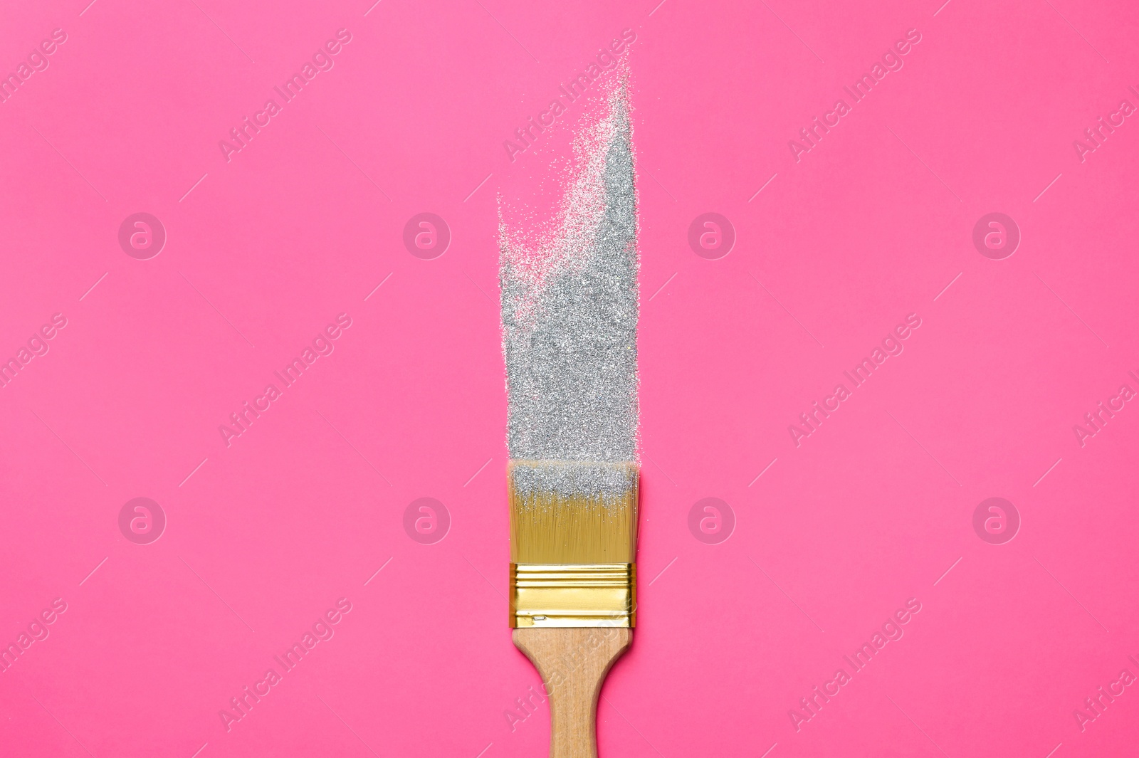 Photo of Brush painting with silver glitter on pink background, top view. Creative concept
