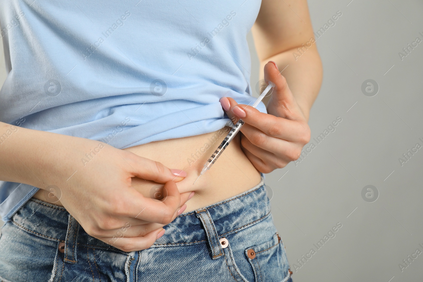 Photo of Diabetes. Woman making insulin injection into her belly on grey background, closeup