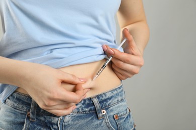 Photo of Diabetes. Woman making insulin injection into her belly on grey background, closeup