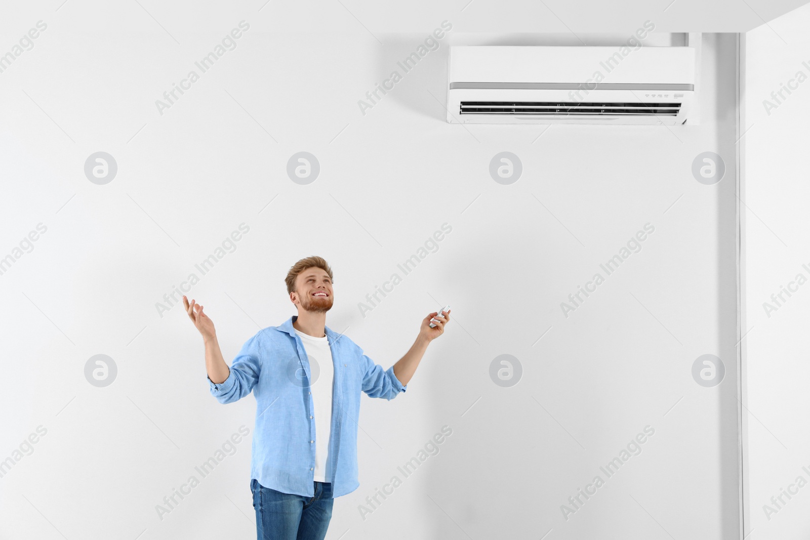 Photo of Young man operating air conditioner with remote control indoors. Space for text