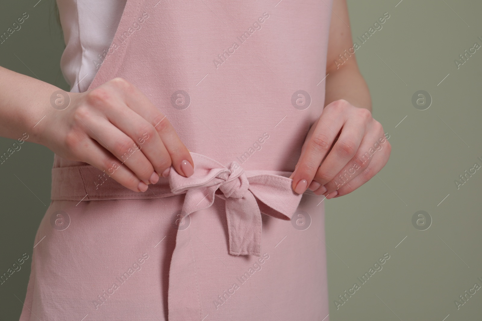 Photo of Woman putting on pink apron against light green background, closeup