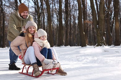 Happy family having fun with sledge in snowy forest. Space for text