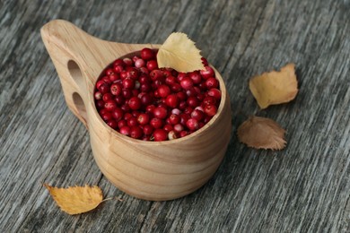 Cup with tasty ripe lingonberries and leaves on wooden surface