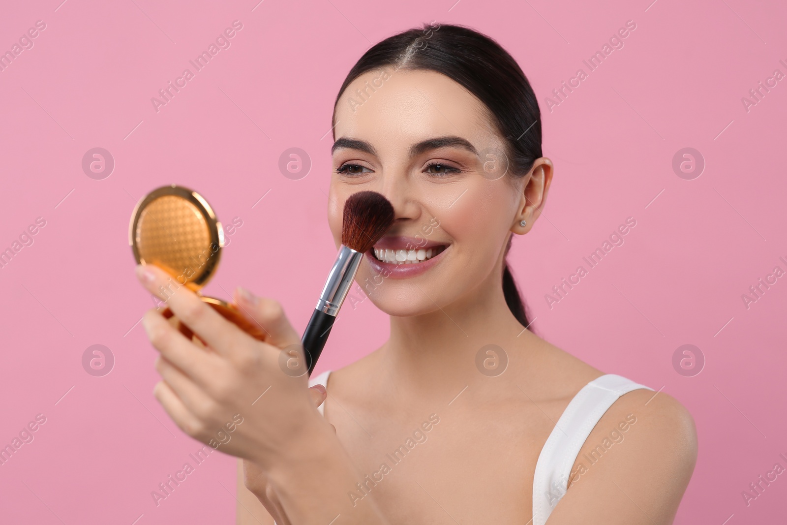 Photo of Beautiful woman with cosmetic pocket mirror applying makeup on pink background