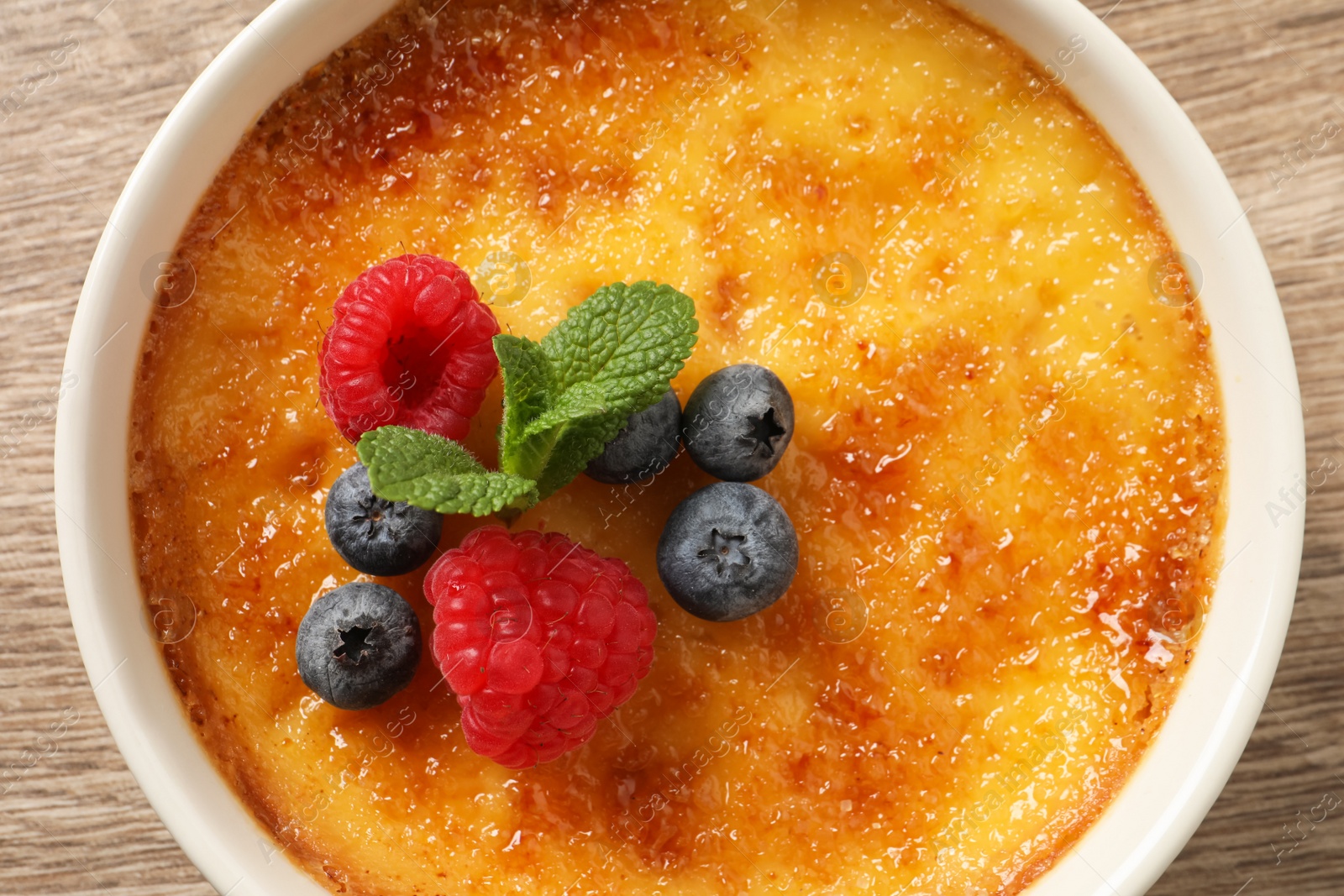 Photo of Delicious creme brulee with fresh berries on wooden table, closeup