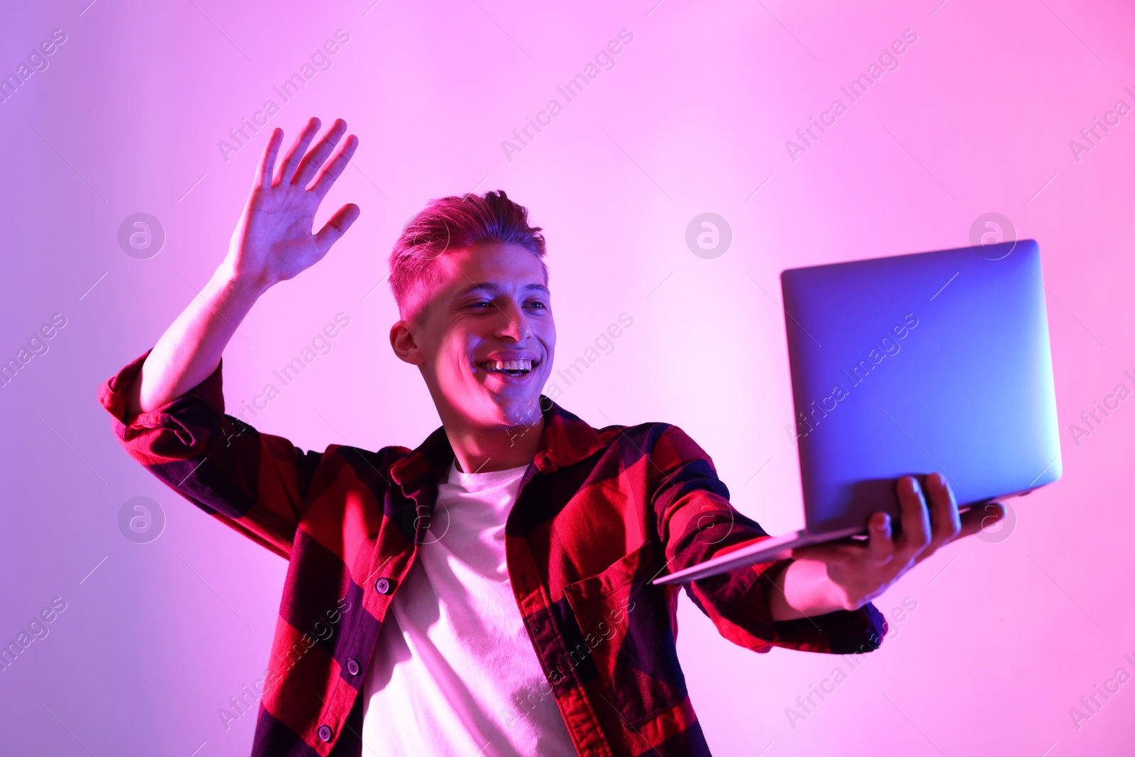 Photo of Young man with laptop talking via video chat on pink background in neon lights