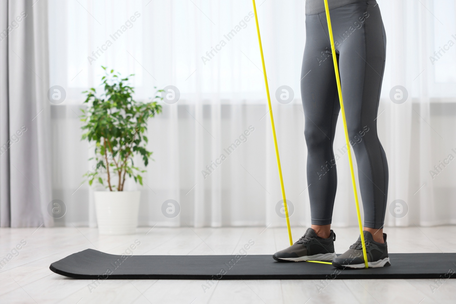 Photo of Woman doing exercise with fitness elastic band on mat at home, closeup. Space for text