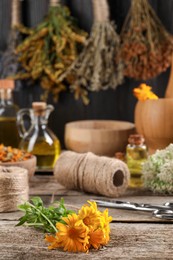 Photo of Calendula flowers, thread and scissors on wooden table, closeup. Medicinal herbs