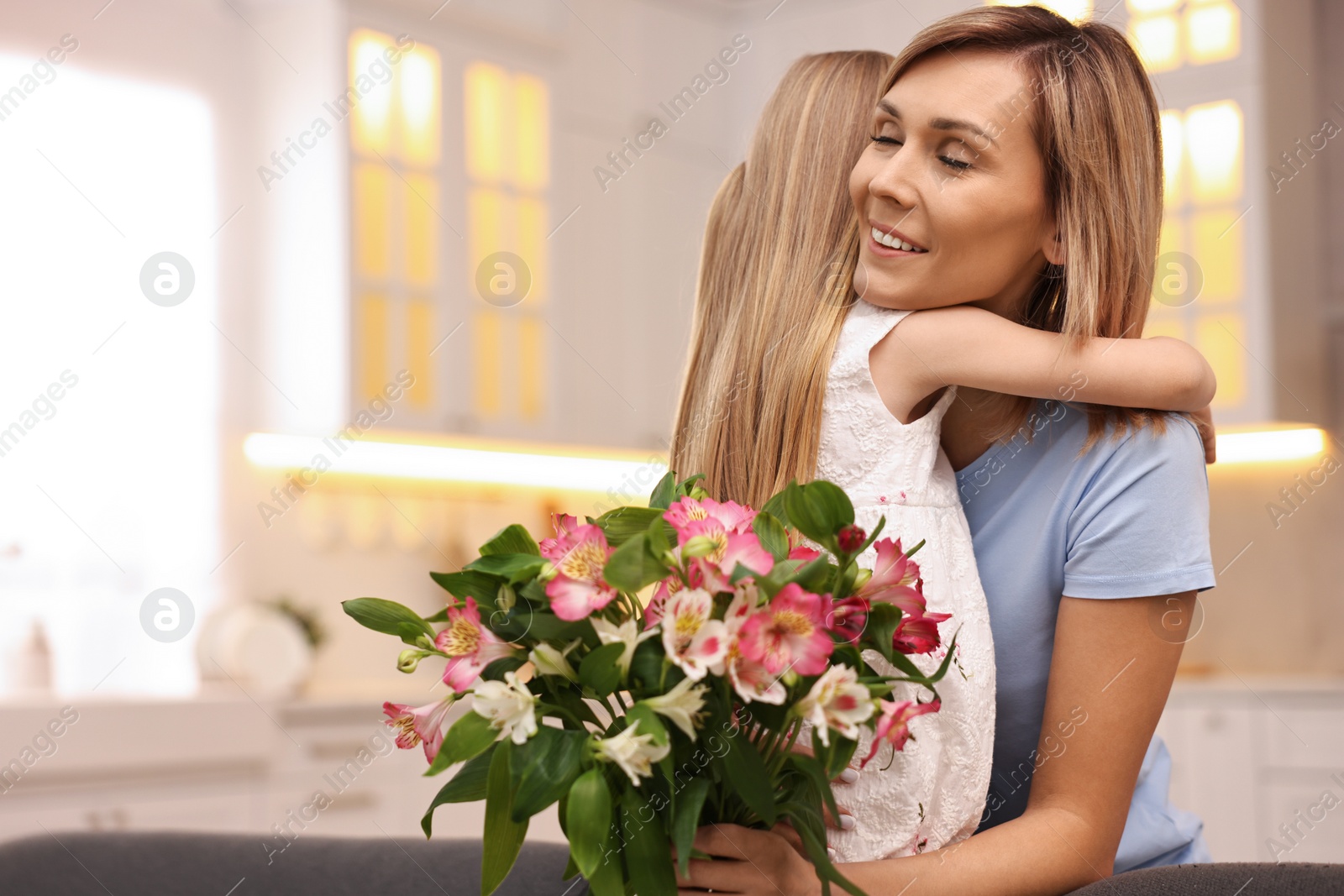 Photo of Little daughter congratulating her mom with bouquet of alstroemeria flowers in kitchen, space for text. Happy Mother's Day