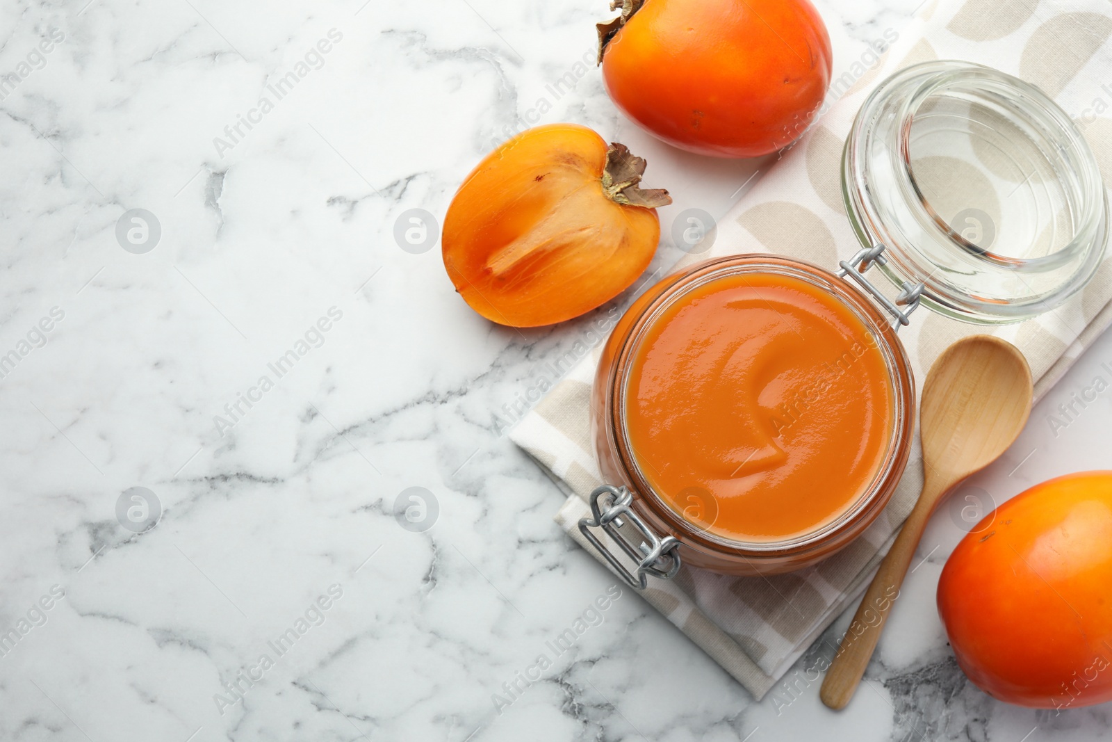 Photo of Delicious persimmon jam and fresh fruits on white marble table, flat lay. Space for text