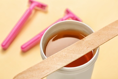 Photo of Jar with sugaring paste and stick on color background, closeup