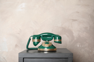 Photo of Green vintage corded phone on small black table near beige wall