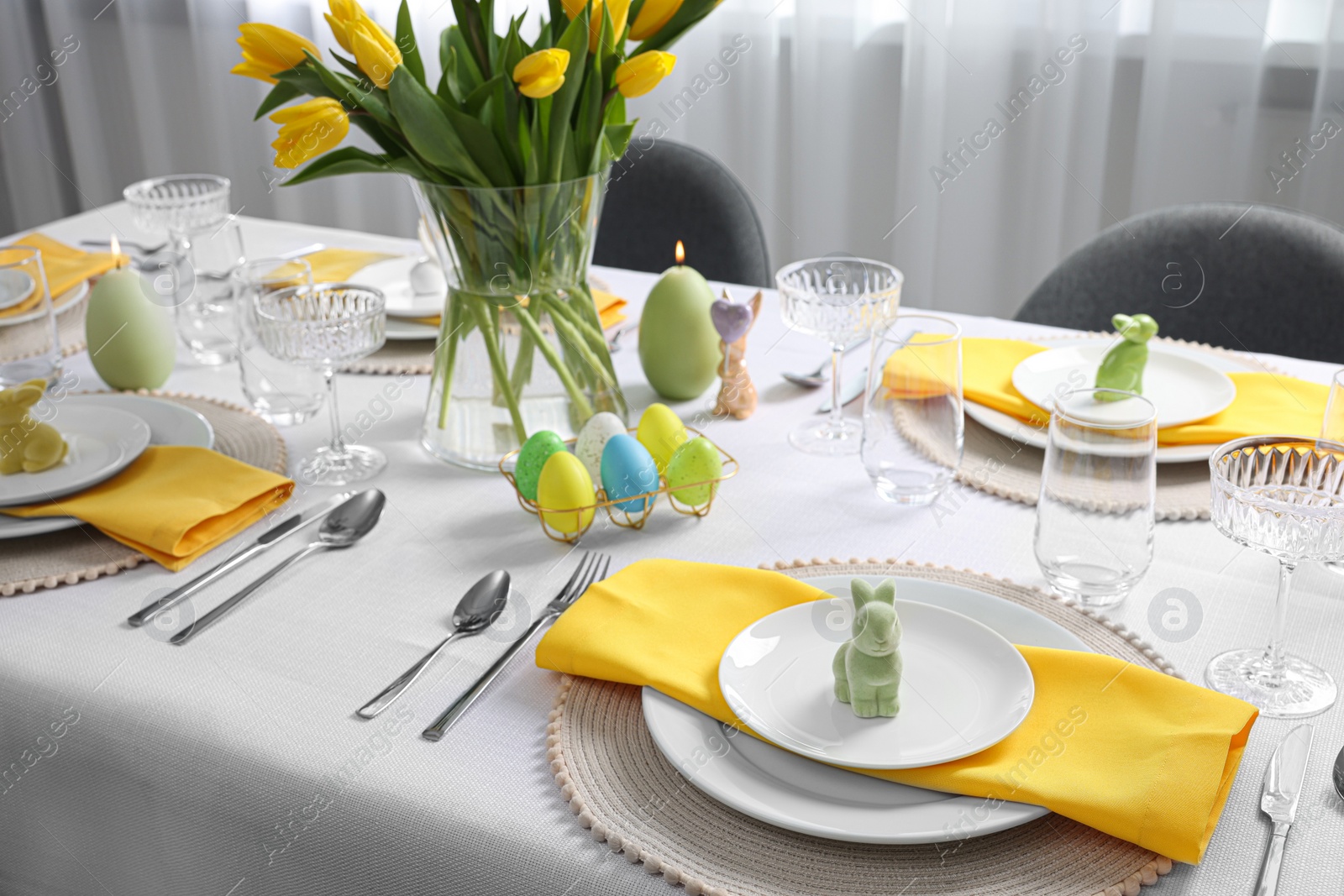 Photo of Festive table setting with glasses, painted eggs and vase of tulips. Easter celebration