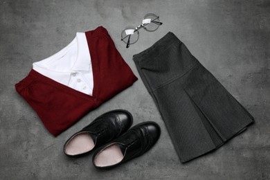 Stylish school uniform for girl and glasses on grey background, flat lay