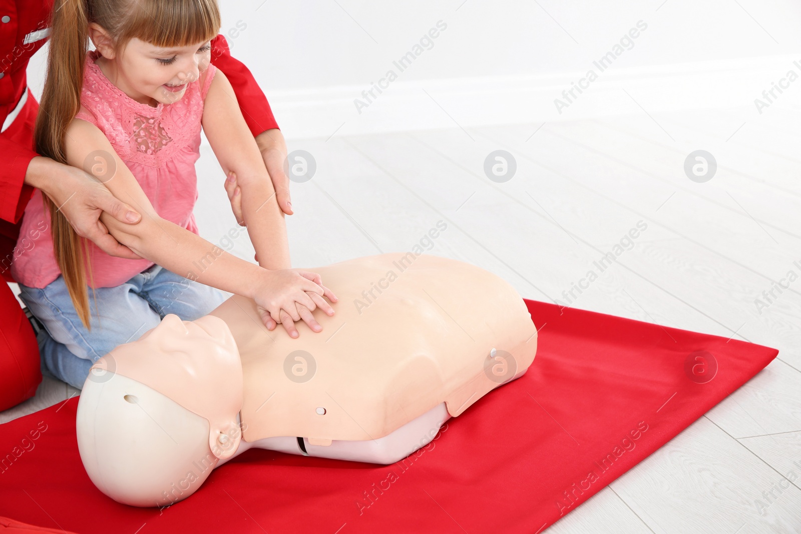 Photo of Instructor with little girl practicing first aid on mannequin indoors, closeup