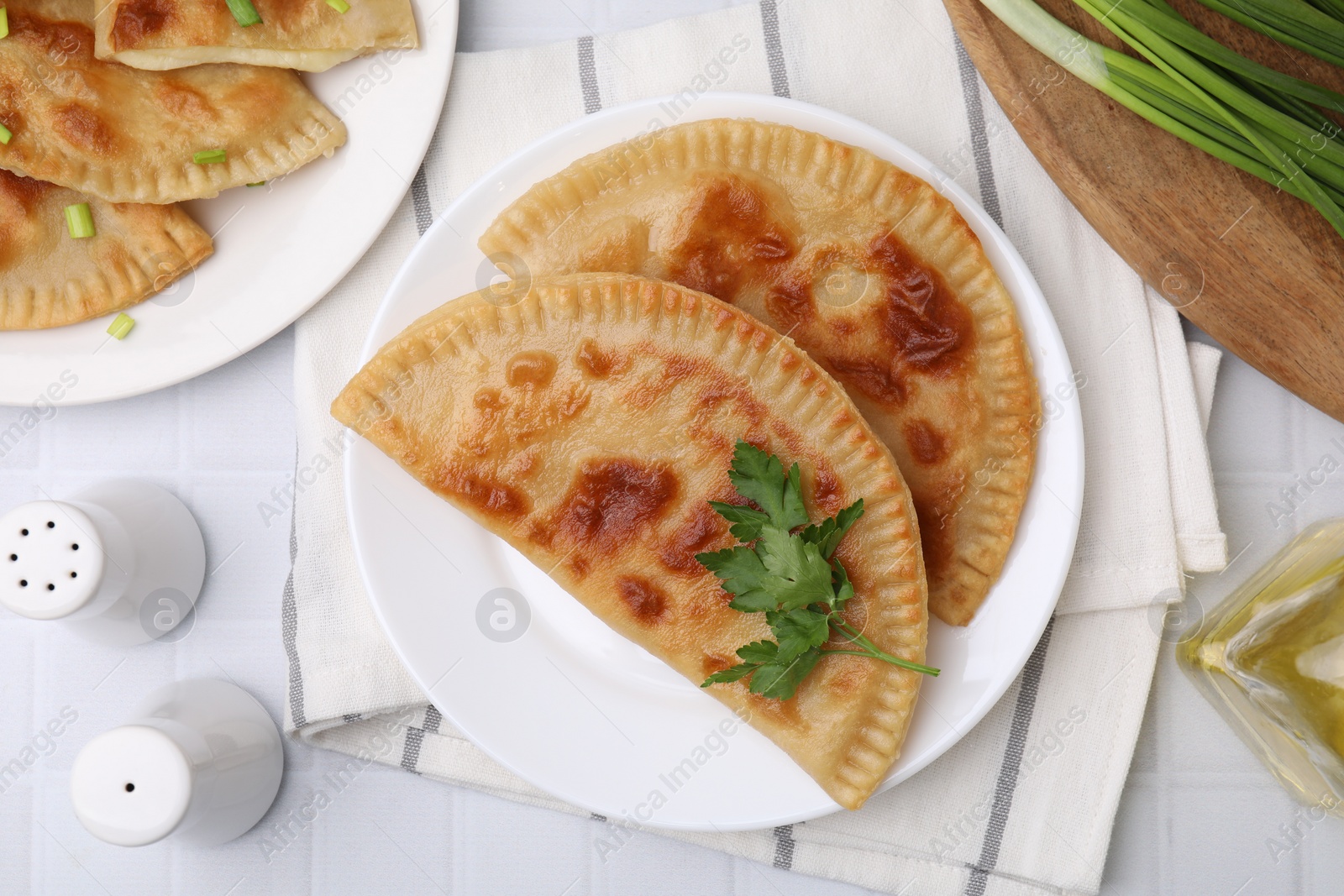 Photo of Delicious fried cheburek with cheese and parsley on white tiled table, flat lay