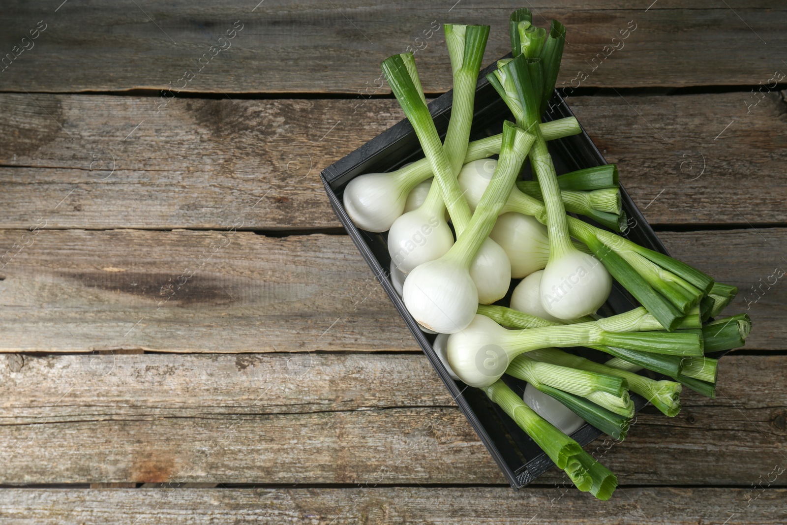 Photo of Black crate with green spring onions on wooden table, top view. Space for text