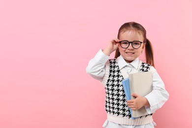 Cute little girl in glasses with books on pink background. Space for text