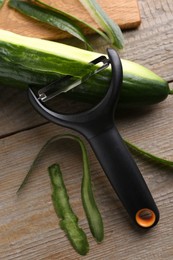 Photo of Fresh cucumber, peels and peeler at wooden table, top view