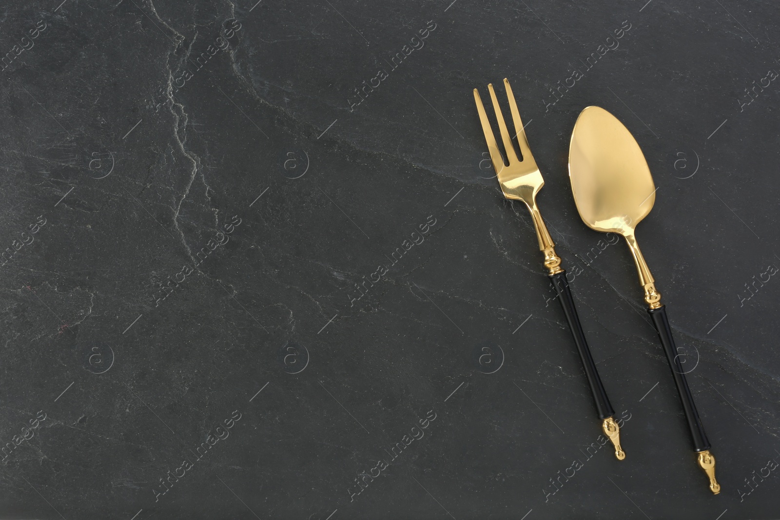 Photo of Shiny fork and spoon on black table, flat lay. Space for text