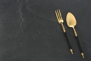 Photo of Shiny fork and spoon on black table, flat lay. Space for text