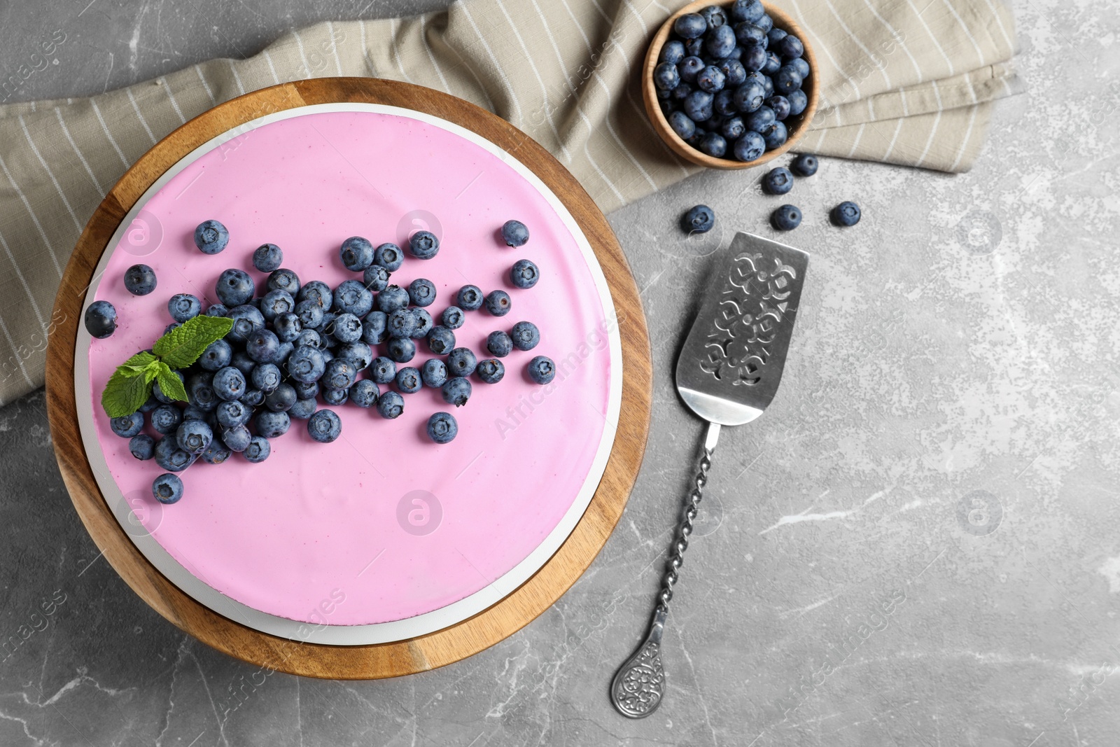 Photo of Wooden stand with tasty blueberry cake on grey table, flat lay. Space for text