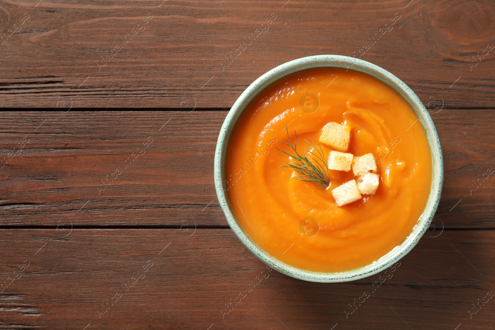 Photo of Bowl of tasty sweet potato soup on wooden background, top view. Space for text