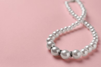 Photo of Elegant necklace with pearls on pink background, closeup. Space for text