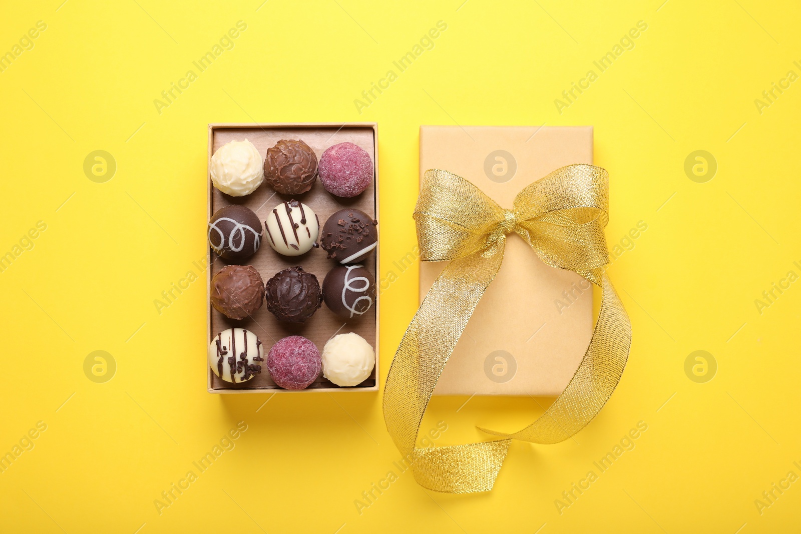 Open box with delicious chocolate candies on yellow background, top view Photo of Open box with delicious chocolate candies on yellow background, top view